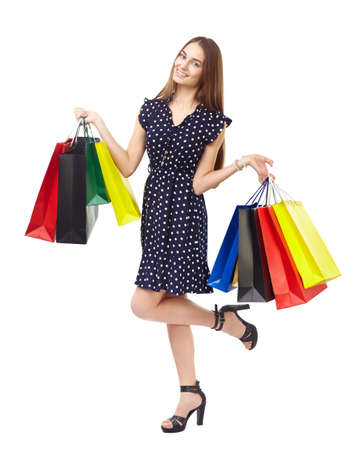 Full length portrait of young beautiful smiling woman holding many colorful shopping bags,standing on one leg, isolated on white backgroundの写真素材