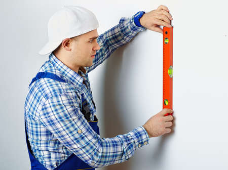 Young construction worker using spirit level on white wallの写真素材