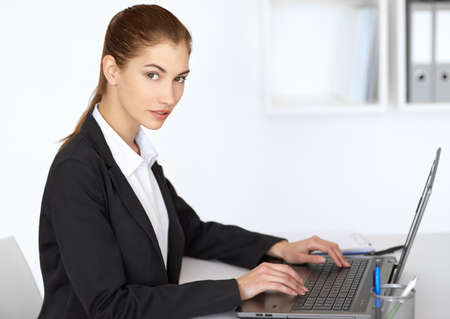 Portrait of beautiful businesswoman sitting at table in office and working at laptopの写真素材