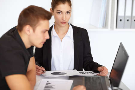Two beautiful young businesspeople sitting at table in office and working with diagram documents and laptopの写真素材