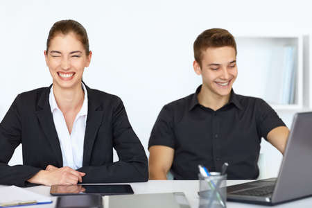 Two young cheerful businesspeople sitting at table in office and laughingの写真素材