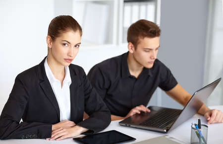 Two beautiful young businesspeople sitting at table in office and working at laptop and tablet pcの写真素材