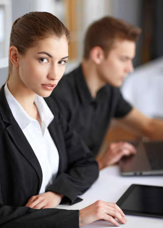 Two beautiful young businesspeople sitting at table in office and working at laptop and tablet pcの写真素材
