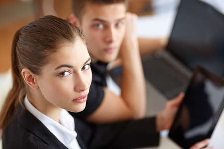 Portrait of two beautiful young businesspeople sitting at table in office and working at laptop and tablet pcの写真素材