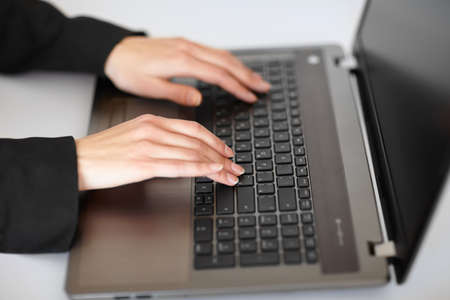 Young businesswoman typing on laptop at table in white office close-up