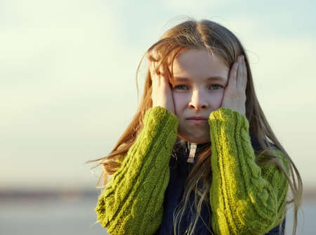 Portrait of sad  little girl holding his head against blue sky backgroundの写真素材