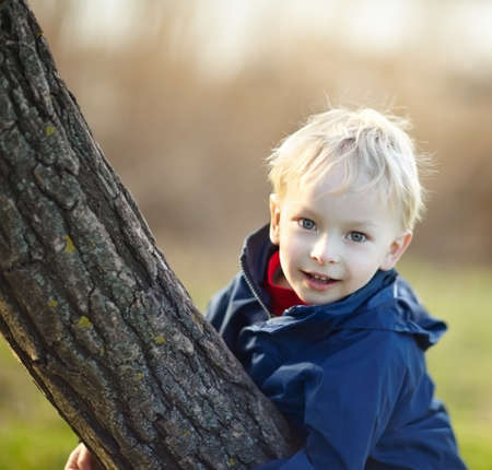 Happy little boy playing near the tree in the spring parkの写真素材