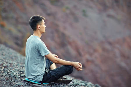 Young man relaxing in yoga position on rocky cliffの写真素材