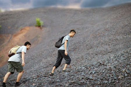 Two young tourist men walks on stones and rock slopeの写真素材