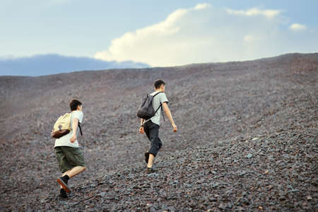 Two young tourist men walks on stones and rock slope