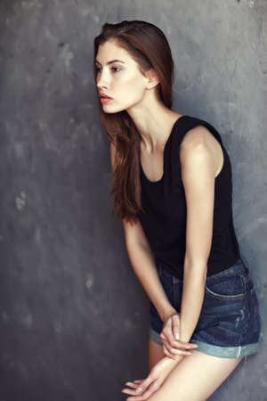 fashion young woman in jeans shorts posing on grunge wall background