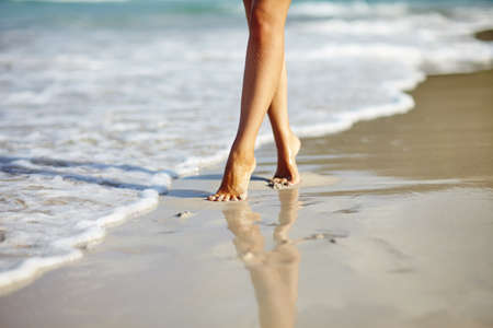 Closeup detail of woman legs and feet walking on the sand of the beach with the sea water in the background. Vacation holiday conceptの写真素材
