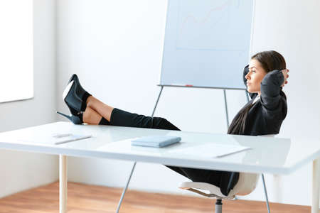 Portrait of relaxed pretty business woman sitting with legs on desk in the office