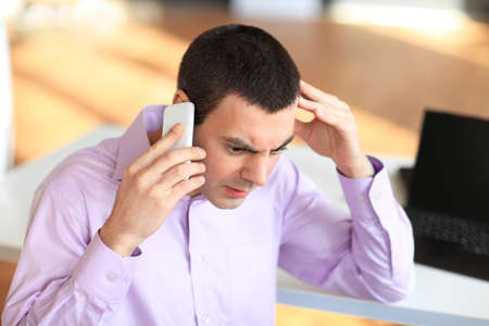 Portrait of young pensive businessman talking on cell phone in officeの写真素材
