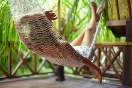 Young beautiful woman relaxing in hammock in a tropical resort.back view