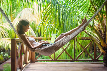 Young beautiful woman lying in a hammock with laptop in a tropical resortの写真素材