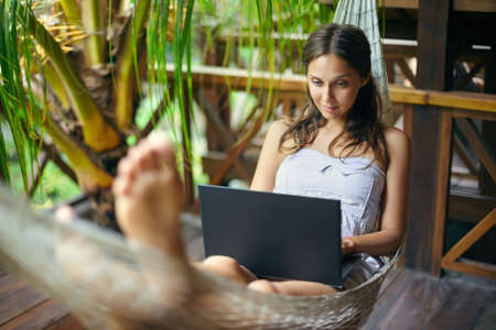 Young beautiful woman lying in a hammock with laptop in a tropical resortの写真素材