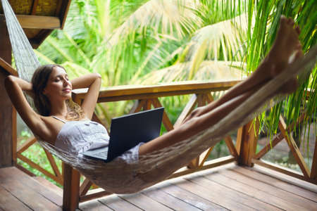 Young beautiful woman relaxing in a hammock with laptop in a tropical resort. Break time