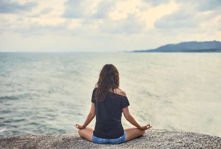 Woman meditating on rocky cliff with sea viewの写真素材