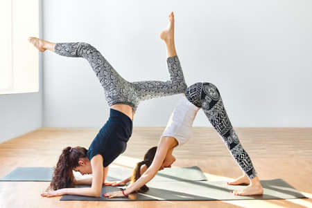 Two young women doing yoga asana downward facing dog. Adho Mukha Svanasana
