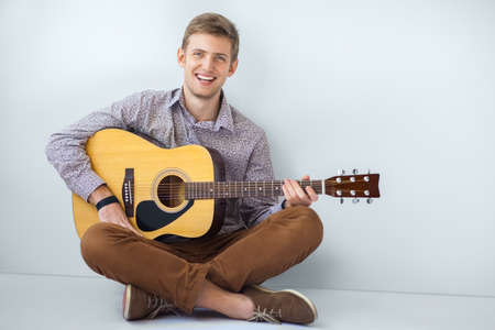 Portrait of happy handsome man playing guitar siting on floorの写真素材