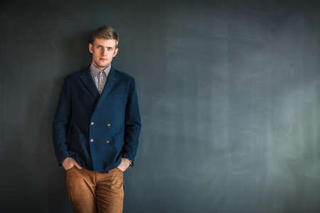 Full length portrait of handsome serious man standing against grey wall background with copy space