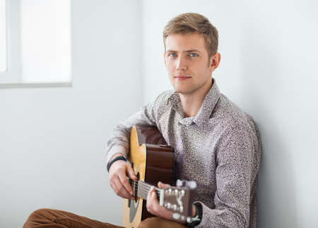 Portrait of handsome man playing guitar siting on floor in studio