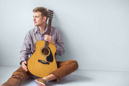 Portrait of handsome man with guitar siting on floor in studio with copy spaceの写真素材