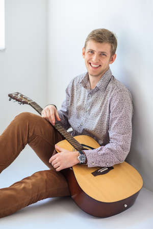 Portrait of handsome smiling man with guitar sitting on floorの写真素材