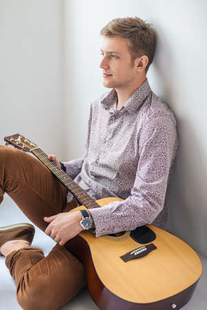 Portrait of handsome man with guitar siting on floor in studioの写真素材