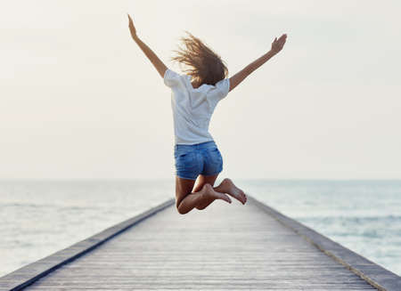 Back view of jumping girl on the pier. Freedom concept