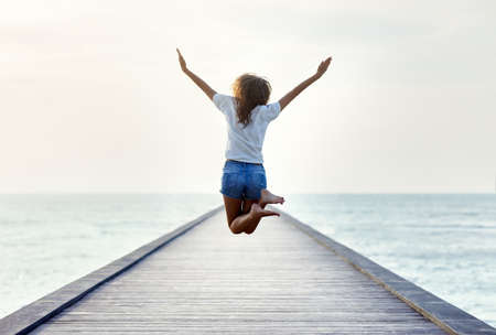 Back view of jumping girl on the pier. Freedom conceptの写真素材