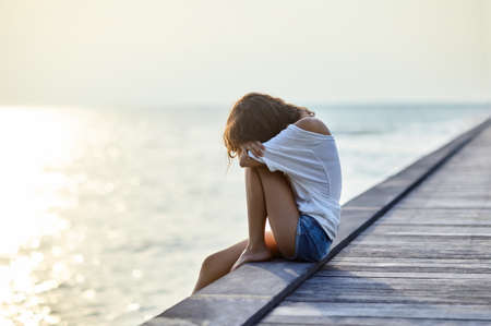 Sad lonely beautiful woman sitting on the pier with copy spaceの写真素材