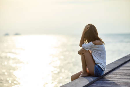 Young beautiful woman sitting on the pier enjoying sunset with copy spaceの写真素材
