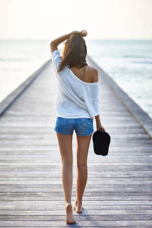 Back view of young beautiful woman walking on the pier. Full length portraitの写真素材