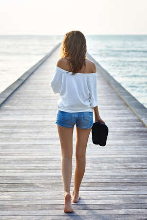 Back view of young beautiful woman walking on the pier. Full length portraitの写真素材