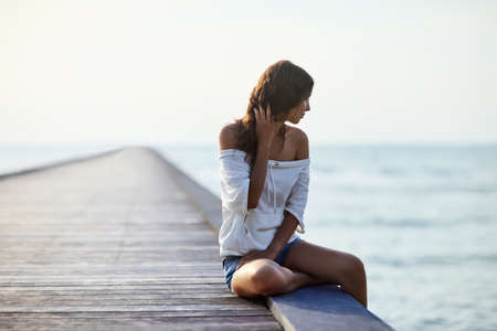 Young beautiful woman sitting on the pier with copy spaceの写真素材