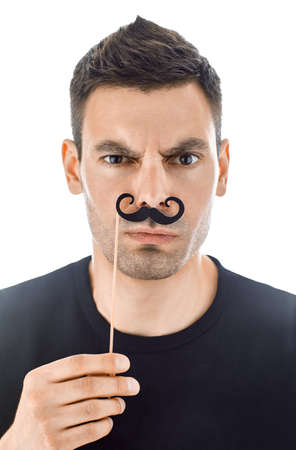 Portrait of young handsome man with paper moustaches making faces isolated on white backgroundの写真素材