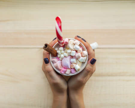 Female hands holding cup of chocolate with marshmallow on rustic wooden table background. Top viewの写真素材