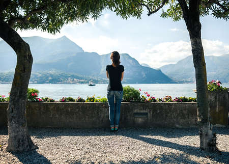 Back view of young woman relaxing on scenic quay of mountain Lake Como in Italy.の写真素材
