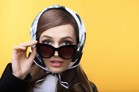 Fashion retro style portrait of beautiful surprised woman in sunglasses on yellow background with copy spaceの写真素材
