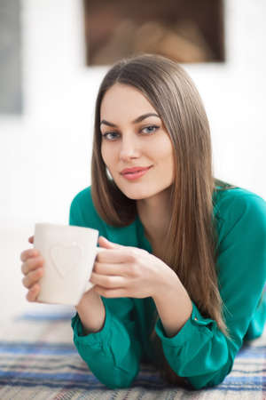 Young beautiful woman lying on plaid with cup of hot coffee in home. Relax conceptの写真素材