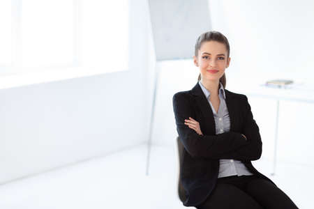 Portrait of young beautiful business woman sitting on chair in the office. Crossed armsの写真素材