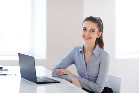 Portrait of young beautiful business woman with laptop in the officeの写真素材