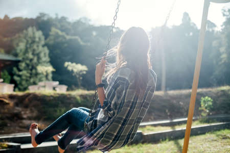 Back view of happy barefoot girl on swing in sun light. Carefree womanの写真素材