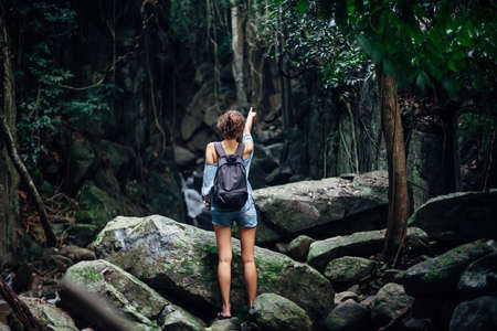 Back view of young woman with backpack in tropical jungle and pointing awayの写真素材