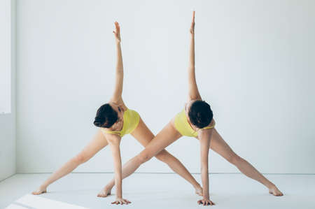 Two young beautiful women doing yoga asana revolved triangle pose variation. Parivrtta Trikonasanaの写真素材