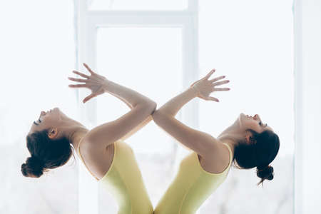 Two young beautiful women doing yoga asana against window