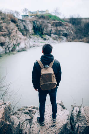 Back view of handsome man standing on rocky cliff and enjoying natureの写真素材