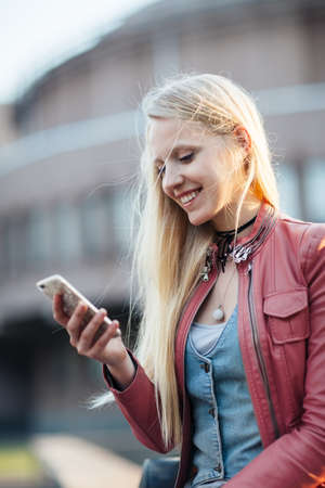 Happy pretty blonde woman using her mobile phone in the streetの写真素材